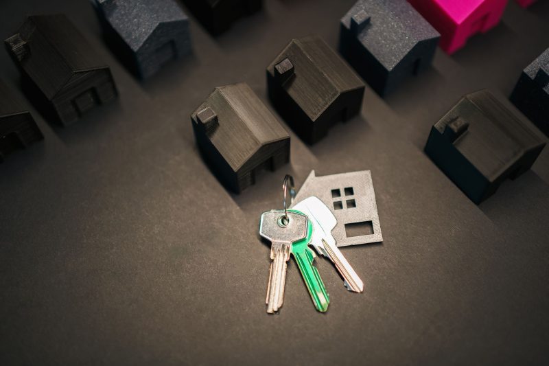 Miniature house models alongside a set of keys on a neutral background.