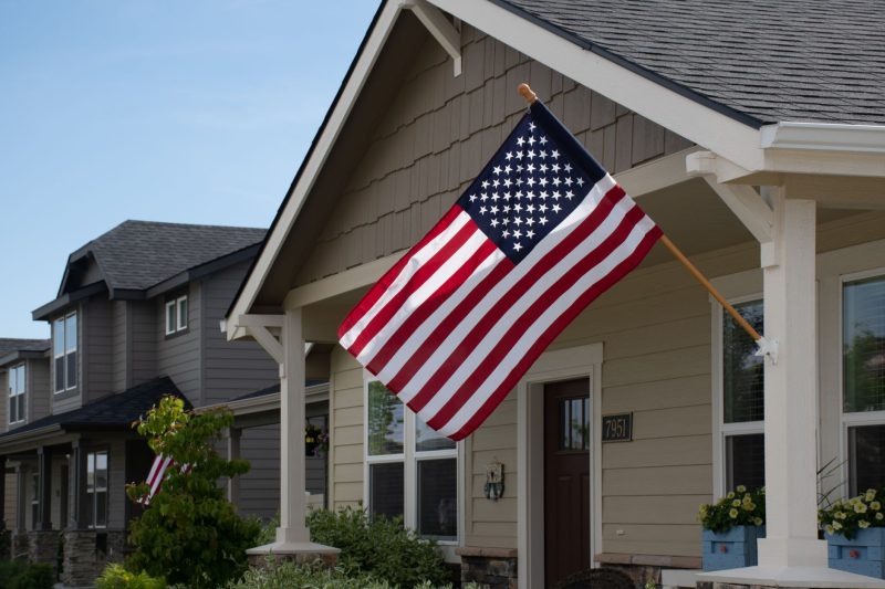 Vibrant American flag fluttering outside a stylish suburban house on a sunny day.