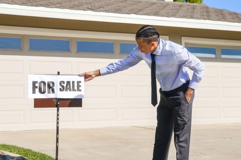 Professional real estate agent placing a "For Sale" sign outside a suburban home.