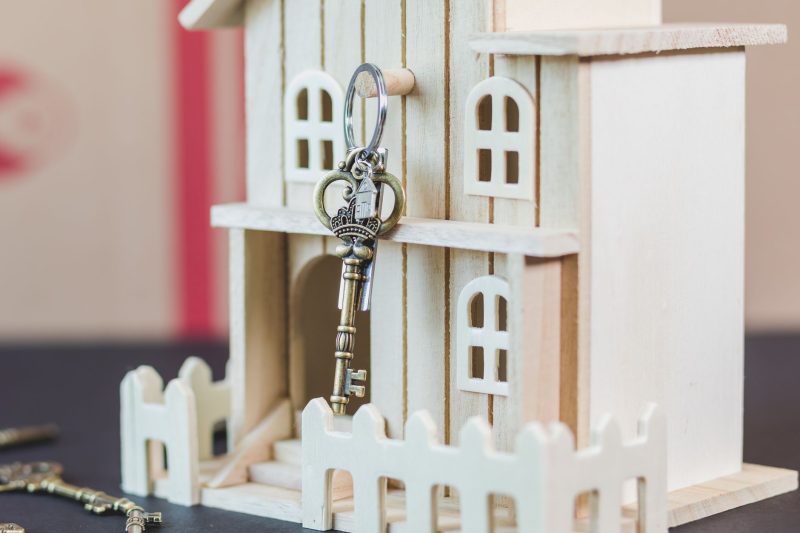 Miniature wooden house beside a vintage key, representing real estate and homeownership.